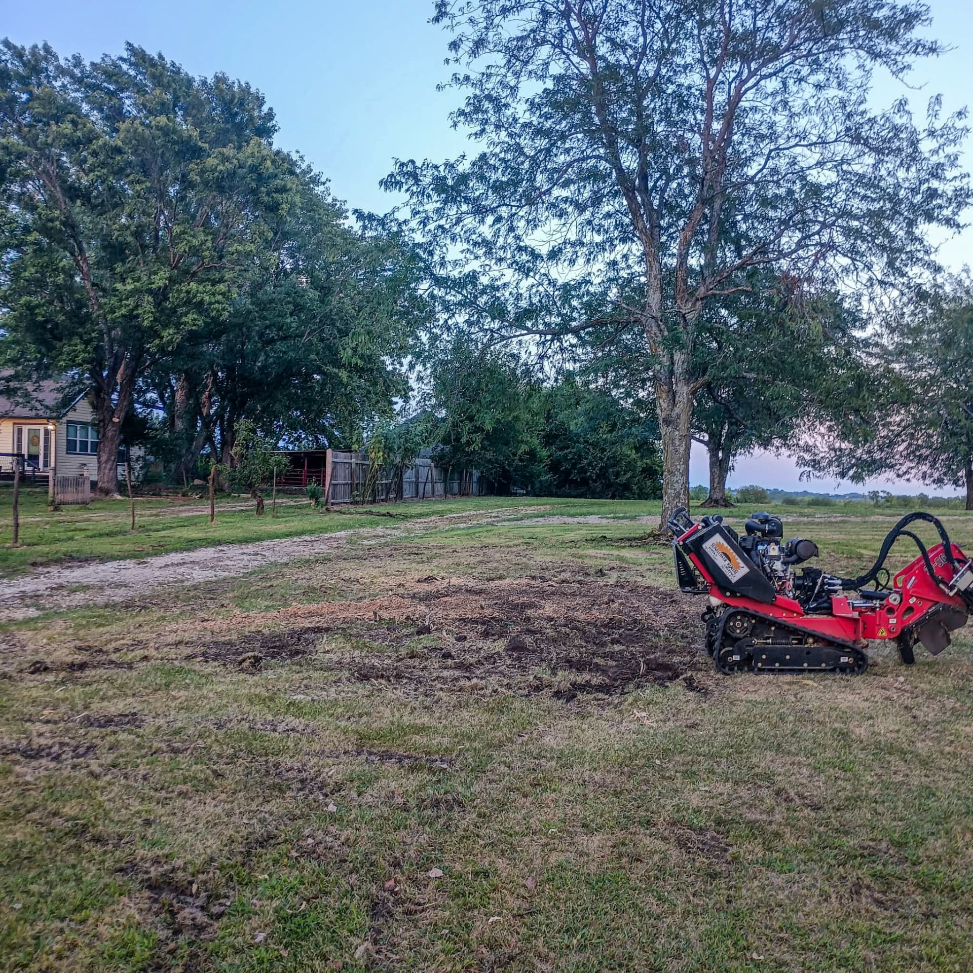 Stump grinding below grade Tracked stump grinder in a cleared grassy yard beside a house